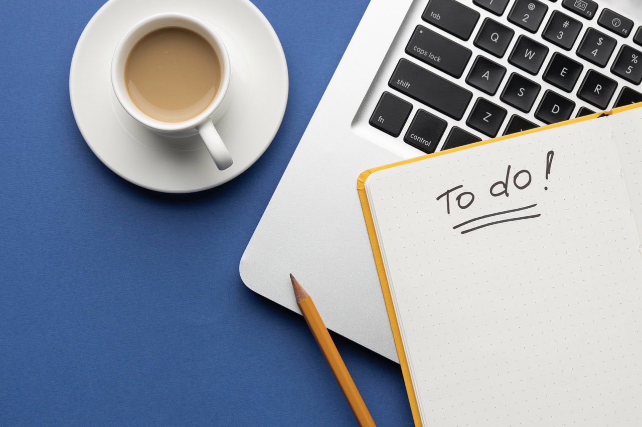 Notatnik z listą postanowień. W tle komputer i filiżanka z kawą